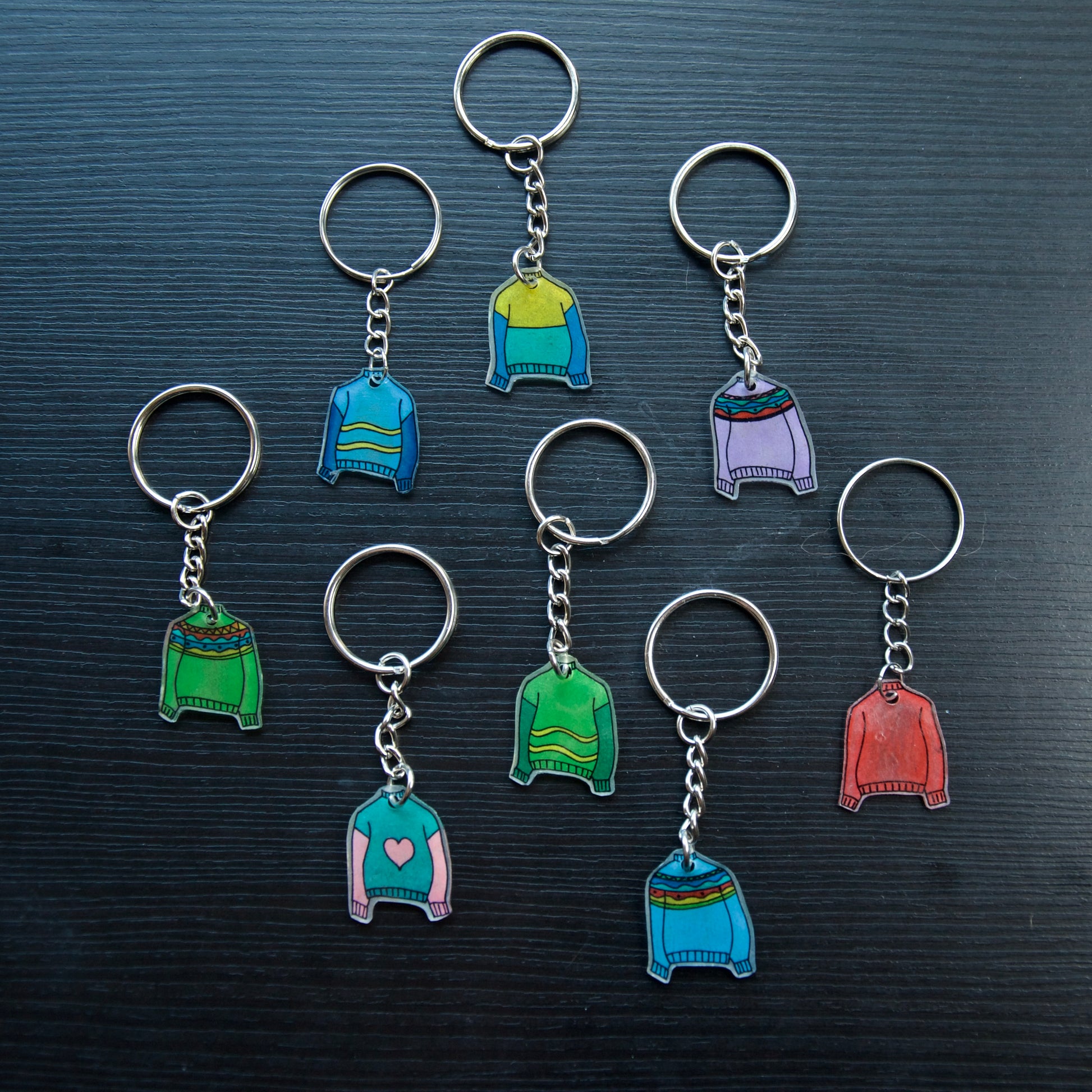 A collection of colorful hand-stitched keychains made from recycled plastic, displayed on a dark surface.