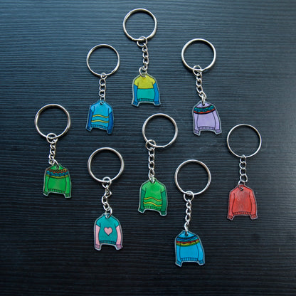 A collection of colorful hand-stitched keychains made from recycled plastic, displayed on a dark surface.