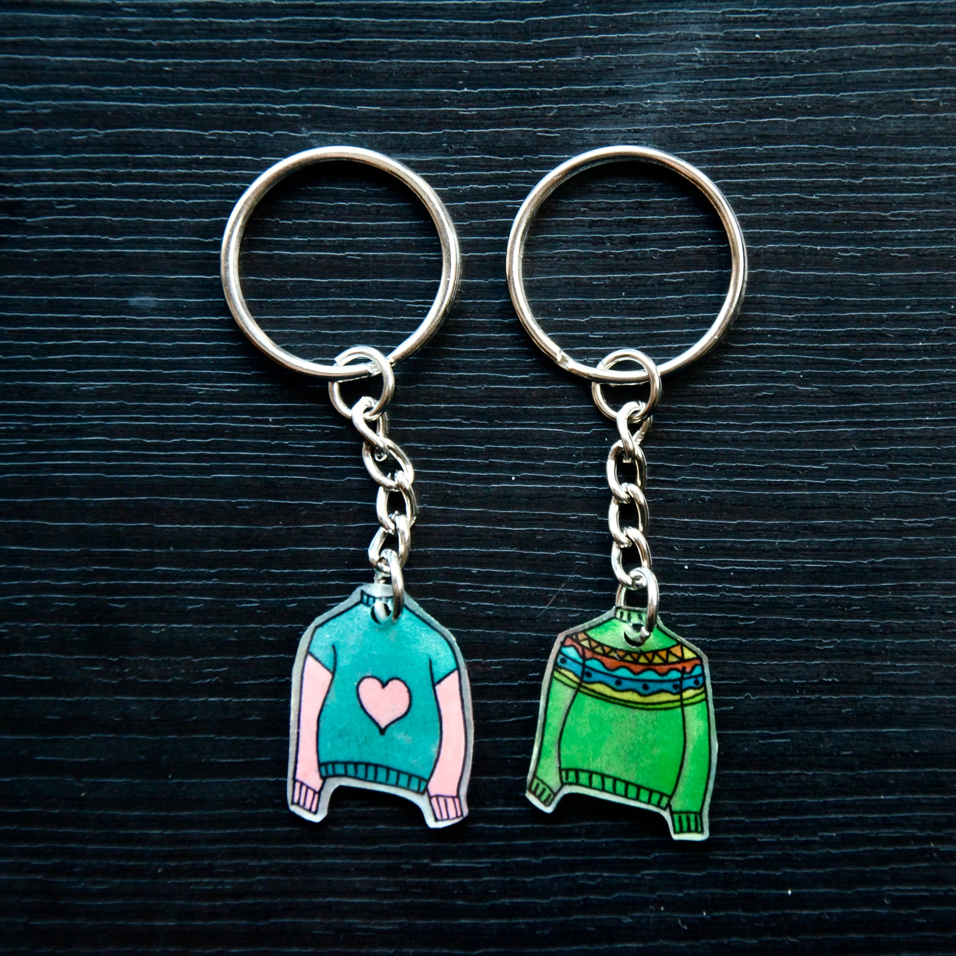 A collection of colorful hand-stitched keychains made from recycled plastic, displayed on a dark surface.