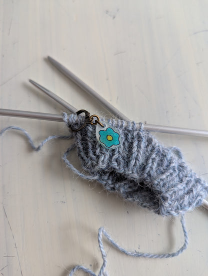 Knitted gray yarn with knitting needles on a light wooden surface, using a hand drawn floral needle minder