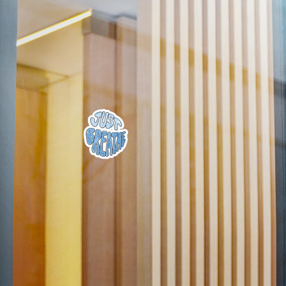 Sticker with 'Just Breathe' text on a glass surface with vertical wooden slats.