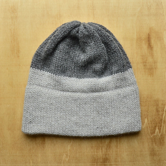 A gray and white striped hand-stitched hat made with alpaca yarn, displayed on a wooden surface.