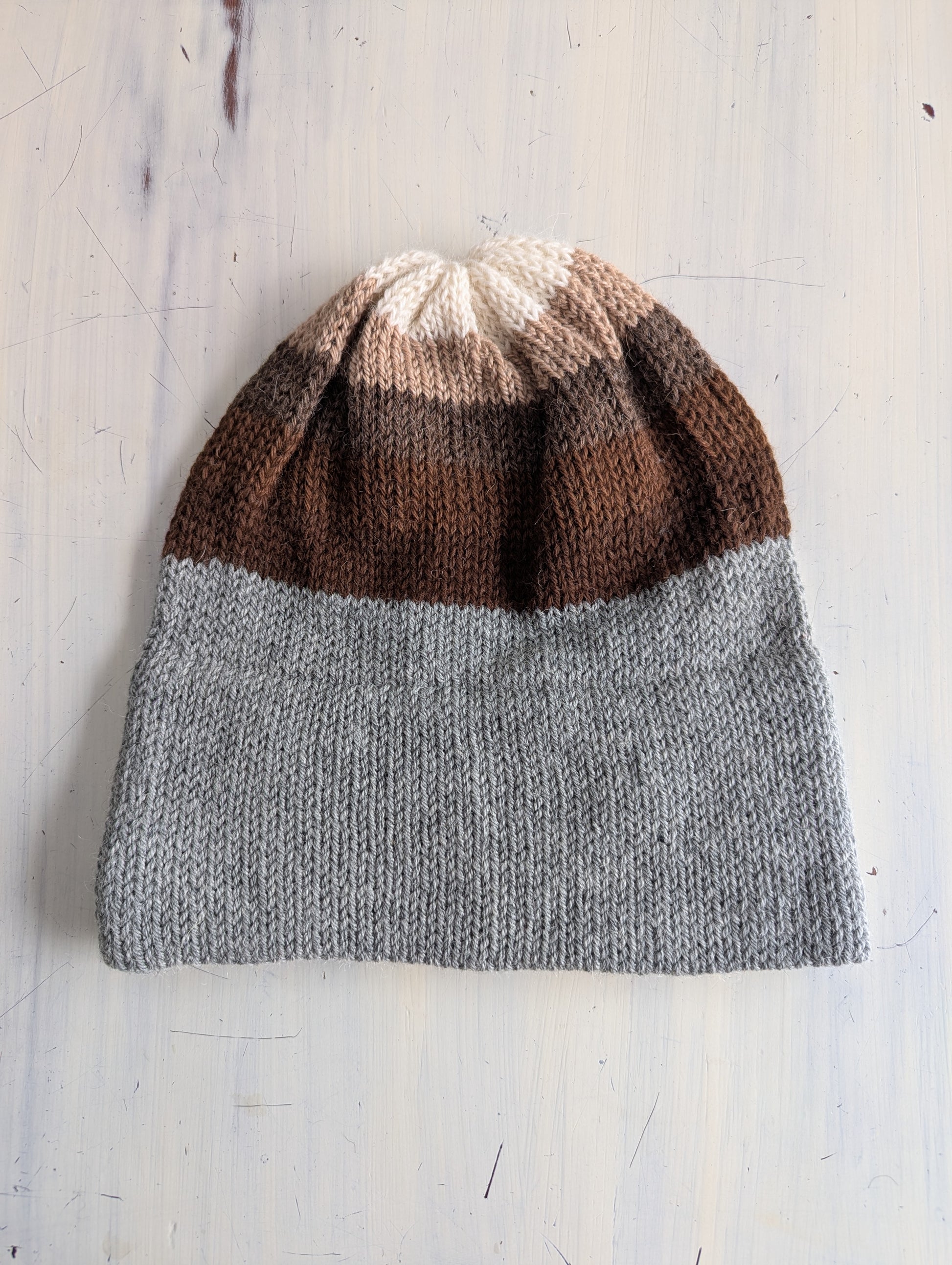 Knitted beanie with brown and gray gradient on a light wooden surface