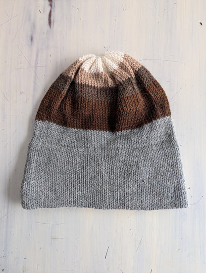 Knitted beanie with brown and gray gradient on a light wooden surface
