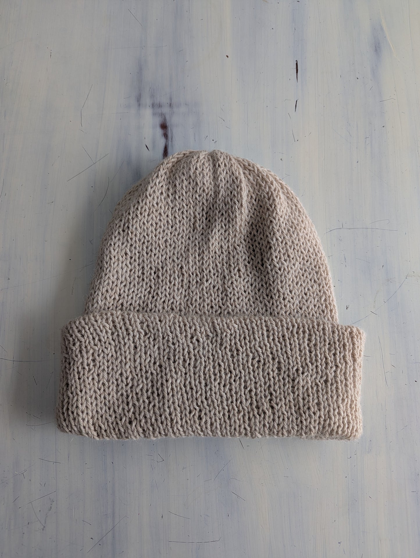 Beige knit beanie on a textured gray background