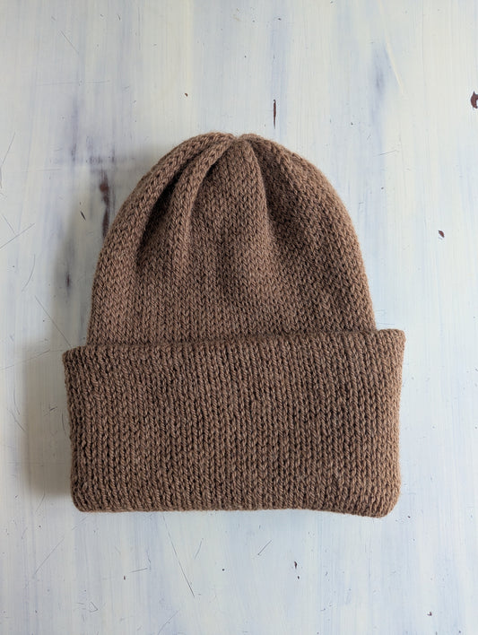 Brown knitted beanie on a light wooden surface