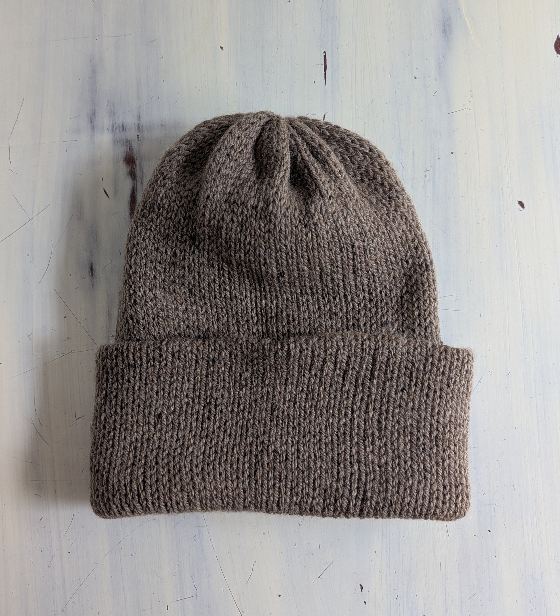 Brown knit beanie on a light blue textured background