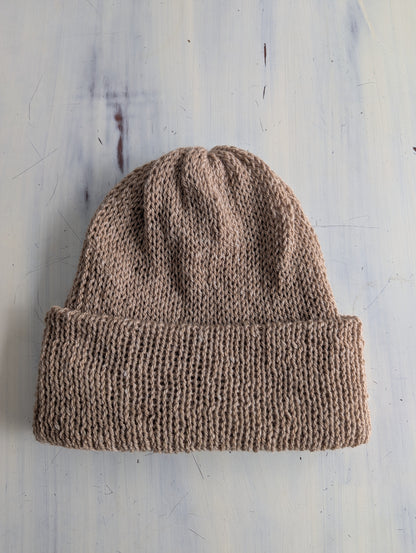 Brown knitted beanie on a textured light gray background