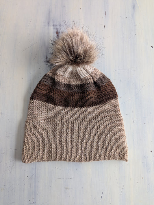 Knitted beanie with a pom-pom on a light wooden surface