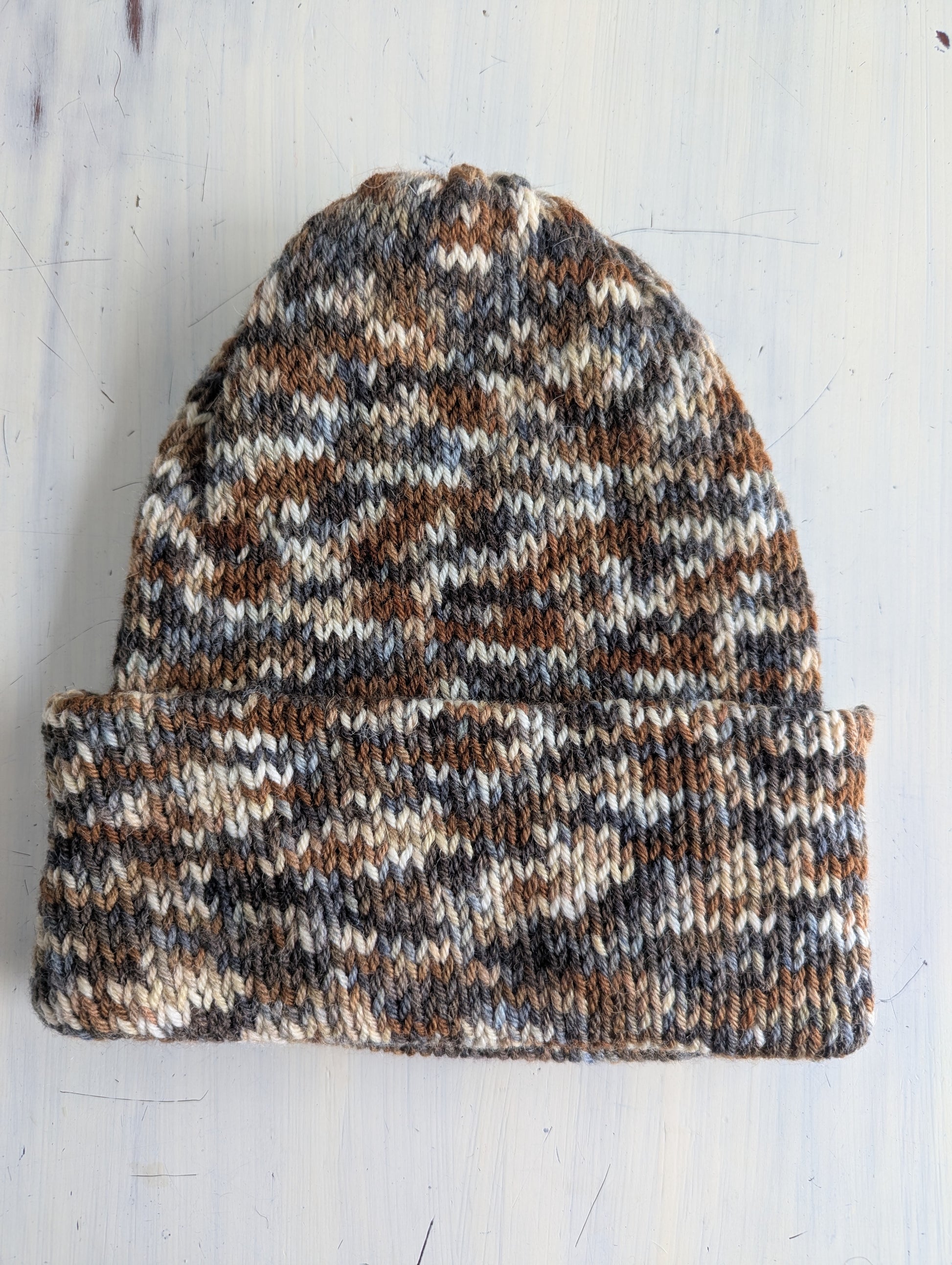Knitted beanie with a camouflage pattern on a light wooden surface