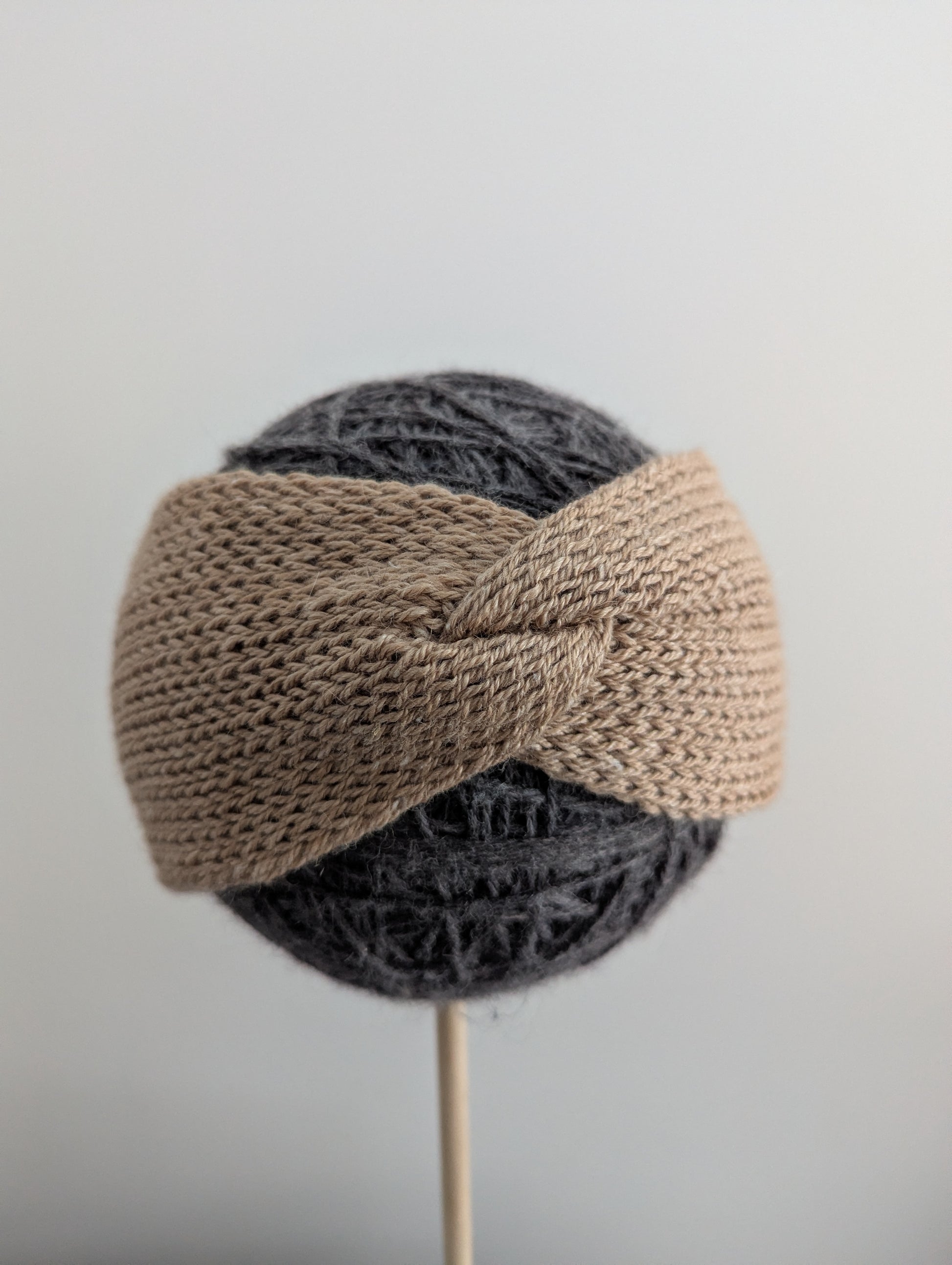 Knitted headband on a mannequin head against a plain background