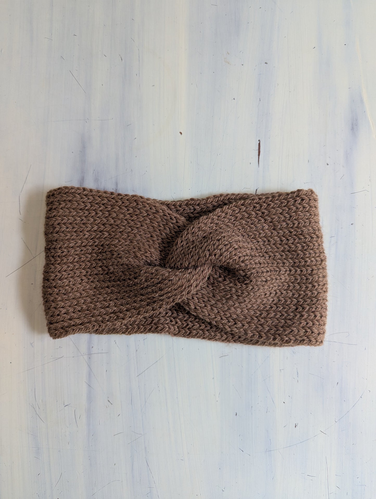 Brown knitted headband on a light grey textured background