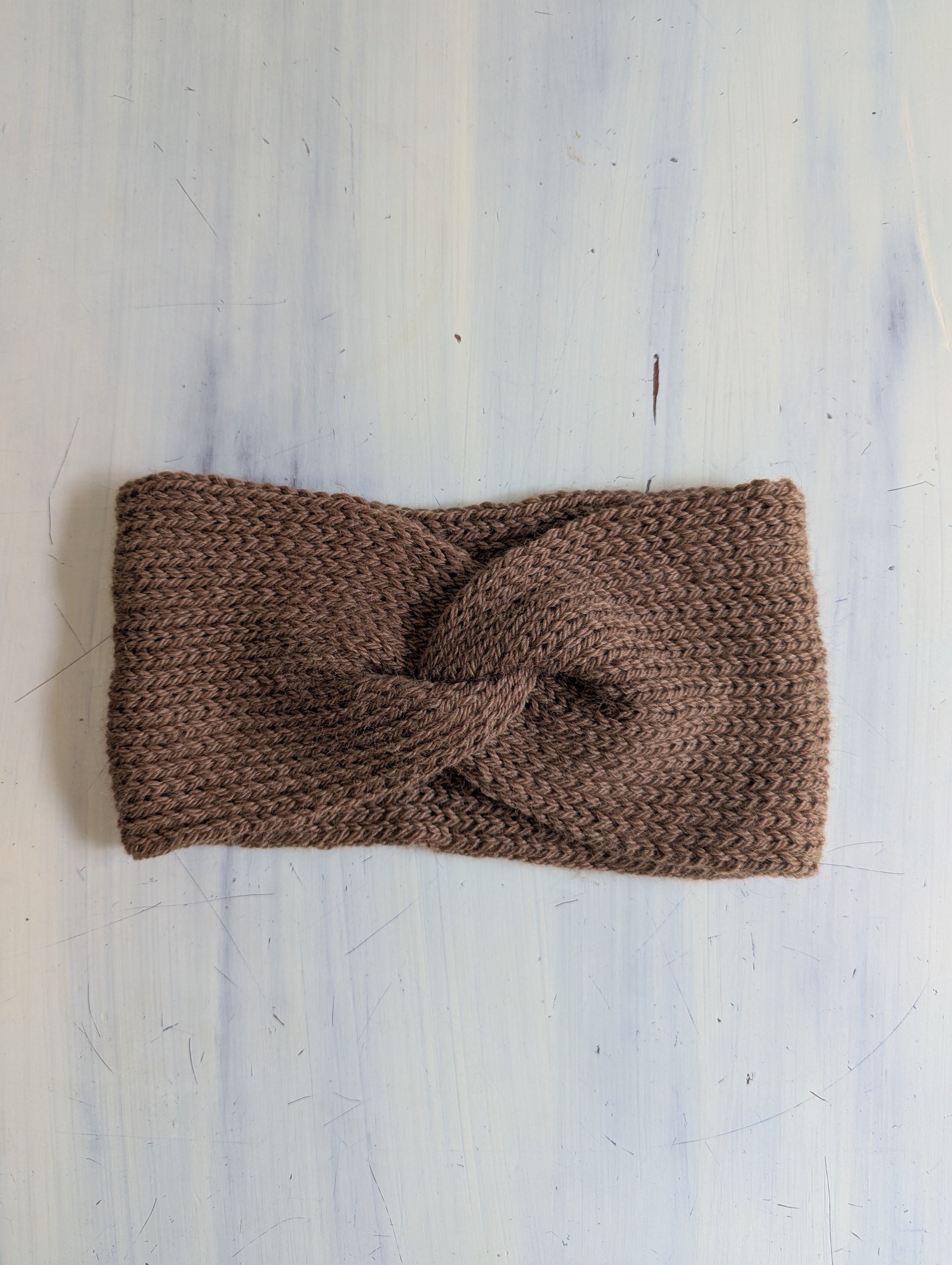 Brown knitted headband on a light grey textured background