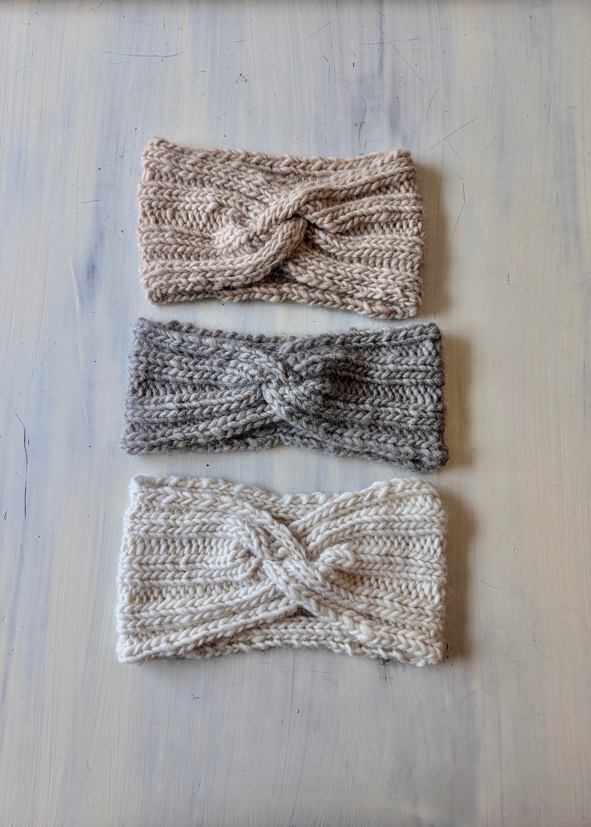 Three knitted headbands in different colors on a light wooden surface