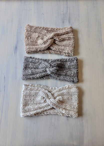 Three knitted headbands in different colors on a light wooden surface
