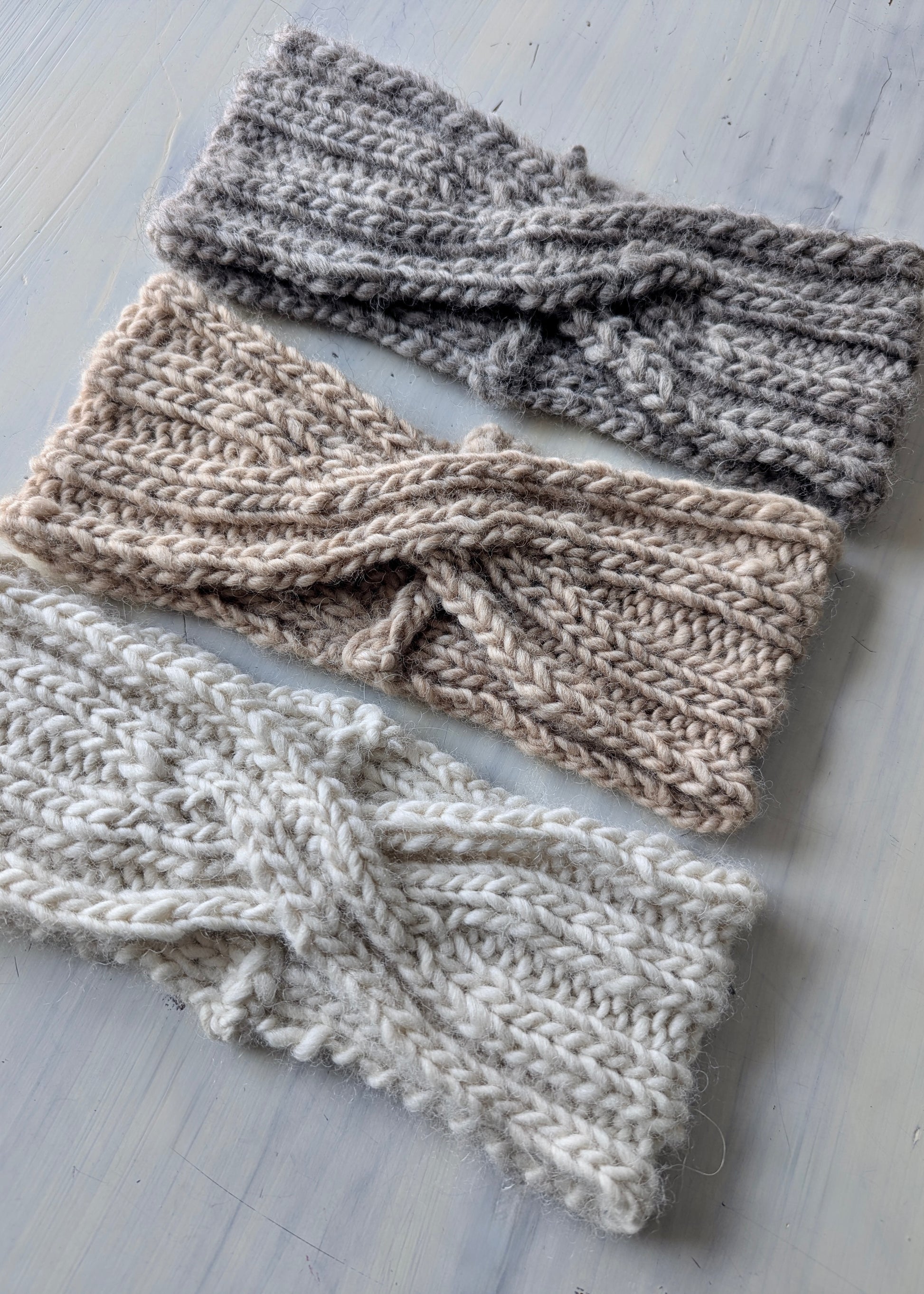 Three knitted headbands in different shades of gray on a light wooden surface.