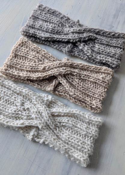 Three knitted headbands in different shades of gray on a light wooden surface.