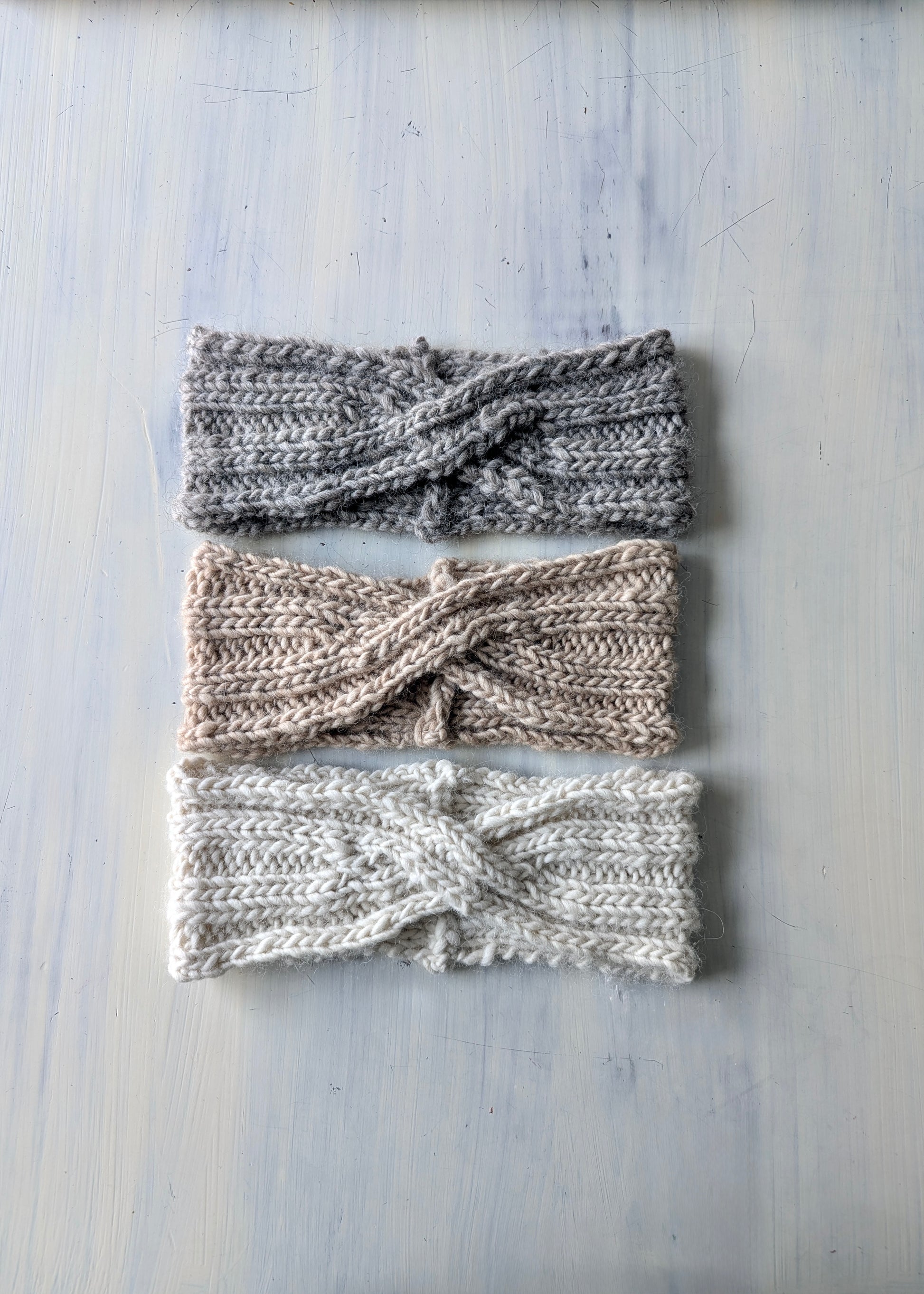 Three knitted headbands of different designs on a light wooden surface.