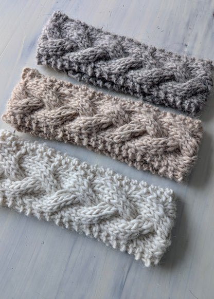 Three knitted headbands in gray, beige, and white on a light wooden surface.