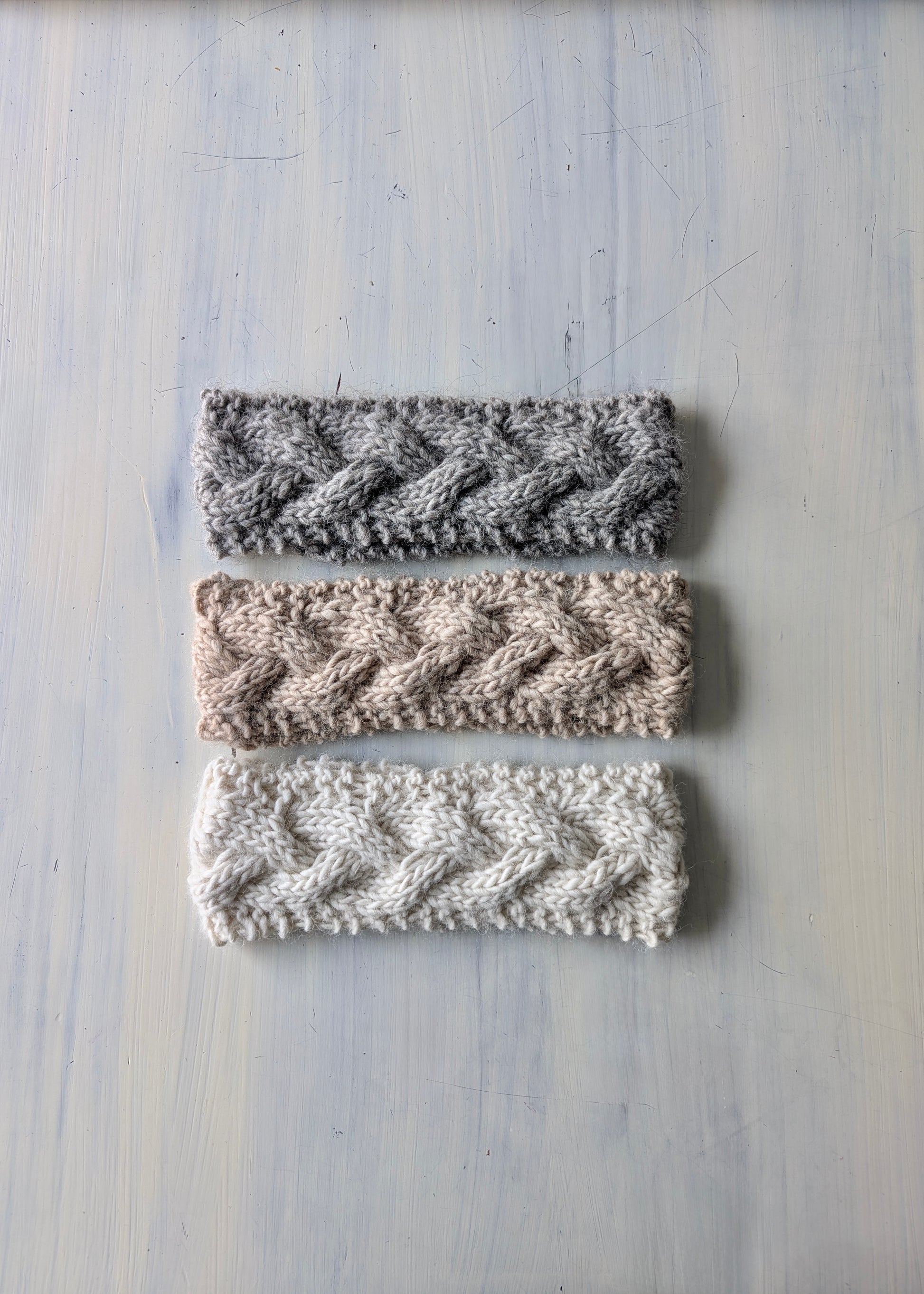 Three knitted headbands in different patterns on a light wooden surface