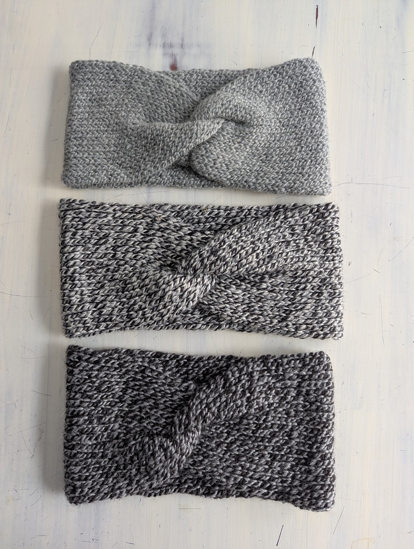 Three knitted headbands in gray and black on a light wooden surface