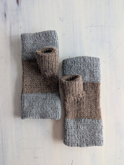 Pair of knitted fingerless gloves with gray and brown color pattern on a light wooden surface.