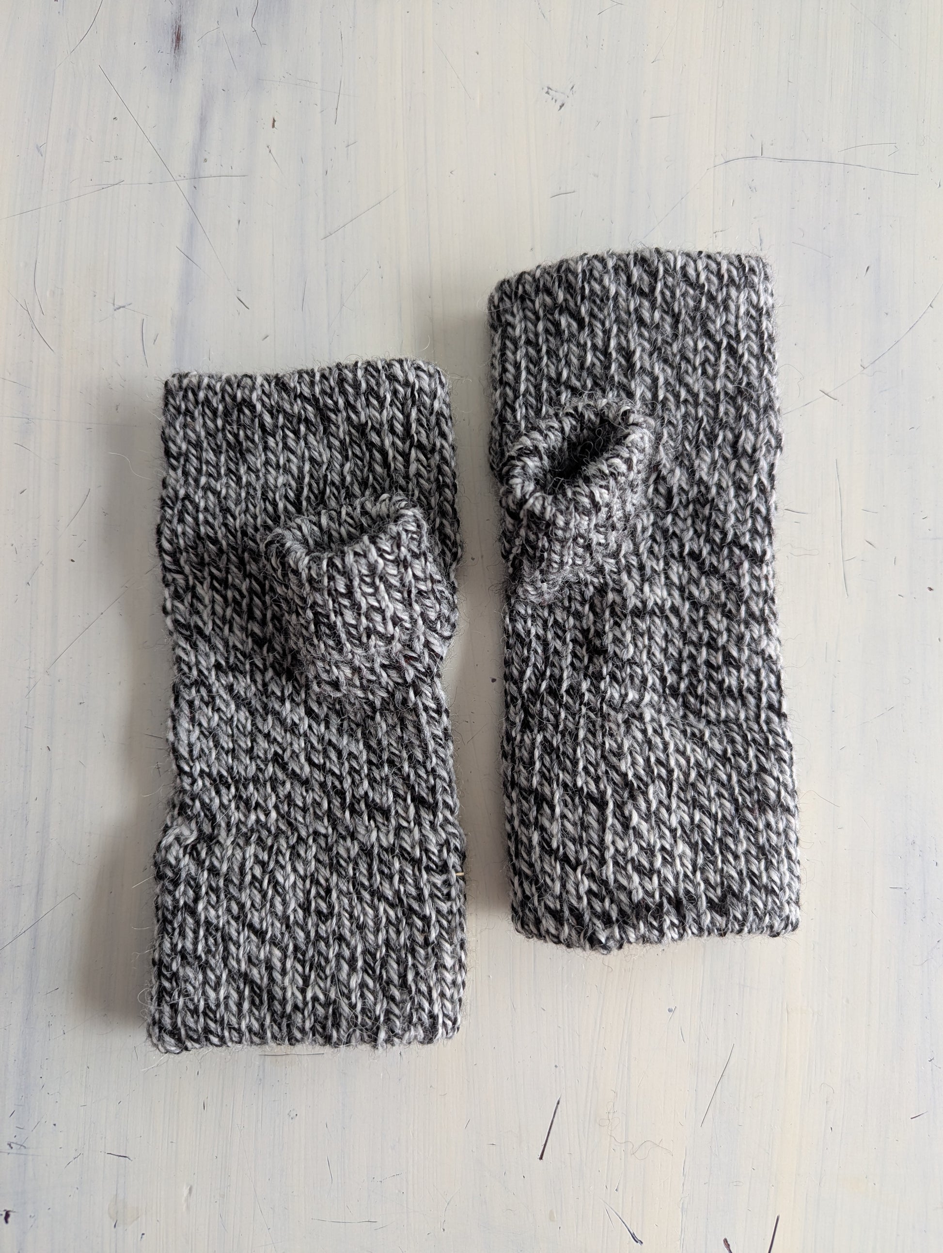 Pair of gray knitted fingerless gloves on a light wooden surface