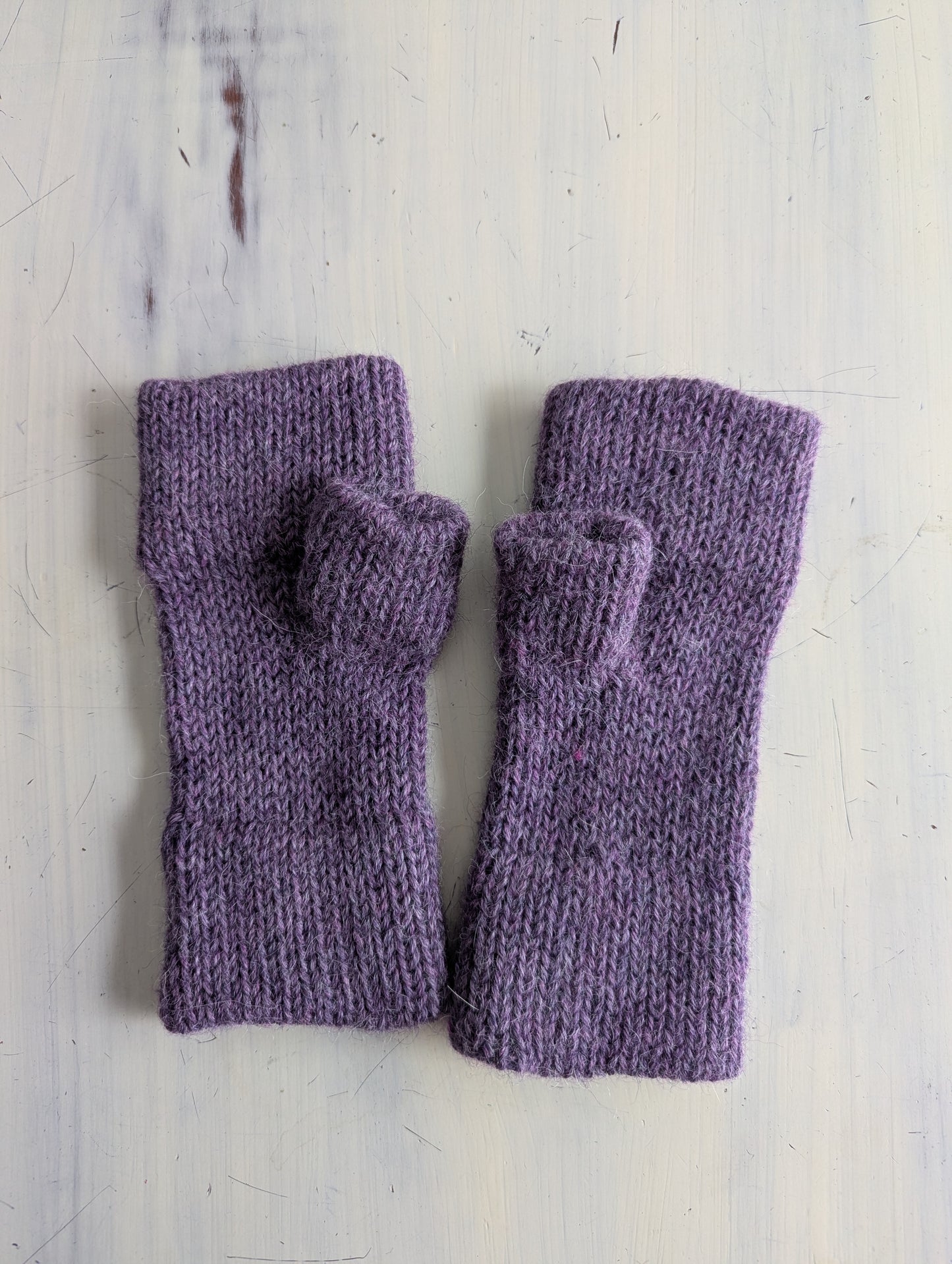 Pair of purple knitted fingerless gloves on a light wooden surface