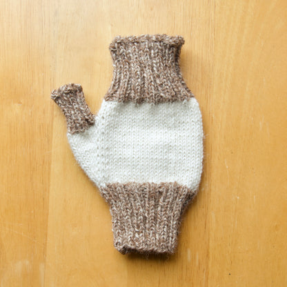 Knit fingerless mitten with white and brown colour pattern on a wooden surface.