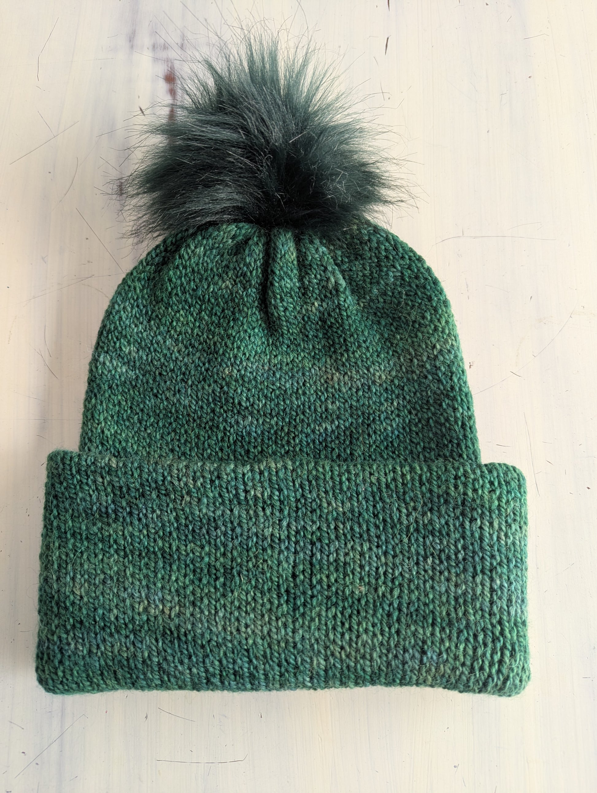 Green knit beanie with a dark green pom-pom on a white background