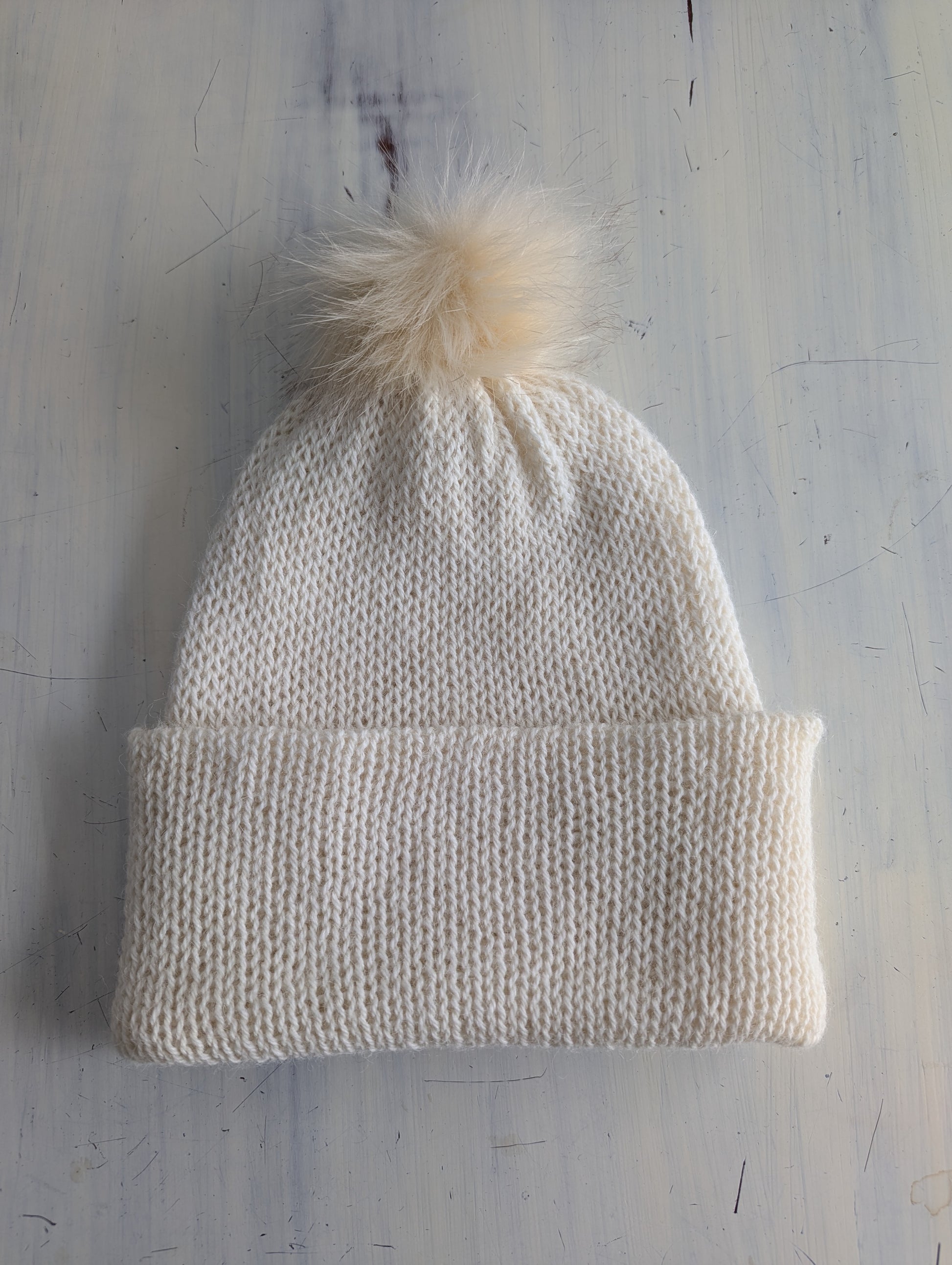Knitted beanie with a pom-pom on a textured light gray background