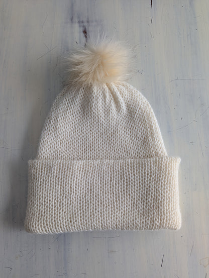 Knitted beanie with a pom-pom on a textured light gray background