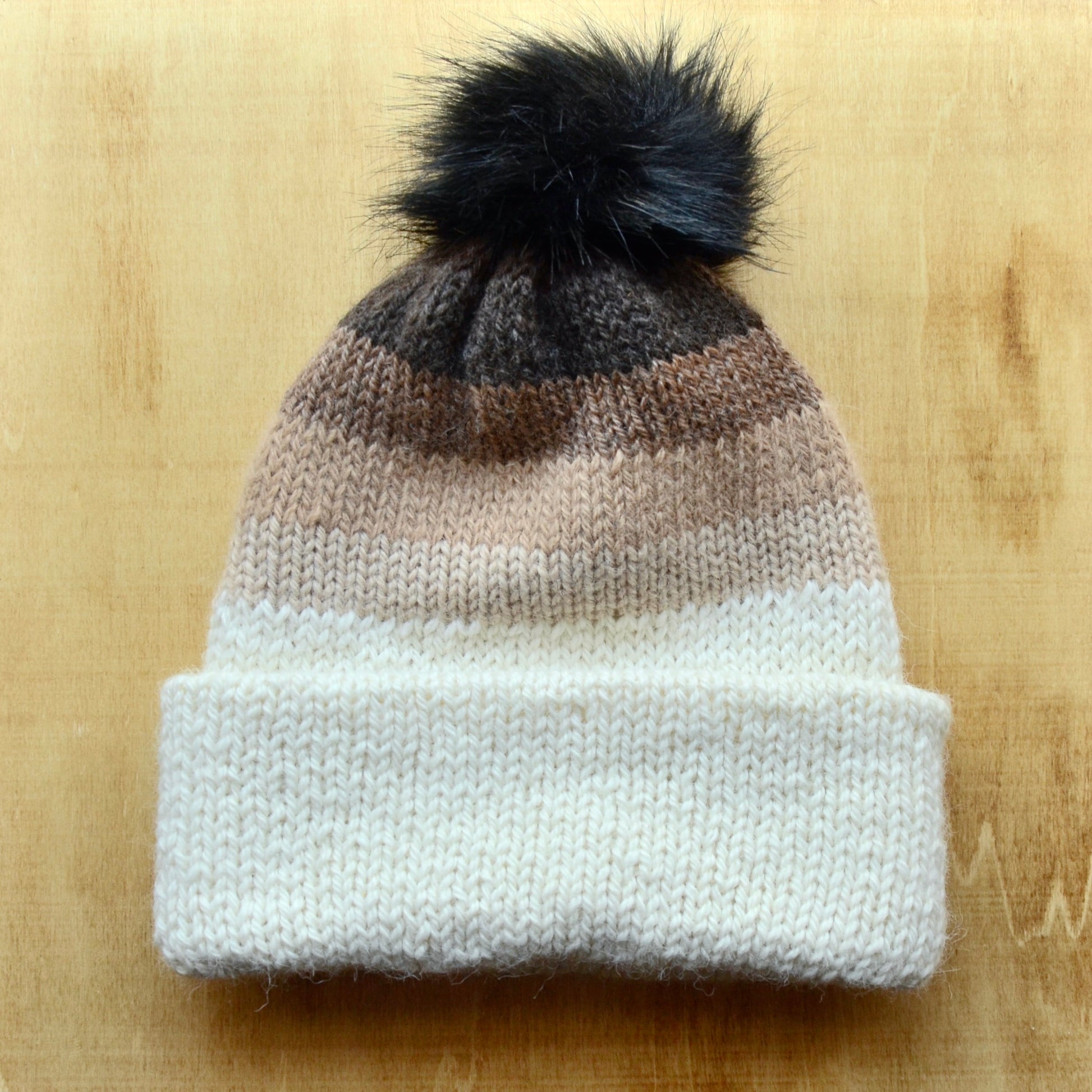 A multicolored beanie with a pom pom on a wooden surface.