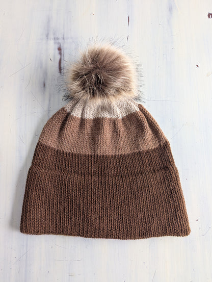 Knitted beanie with a fur pom-pom on a light wooden surface