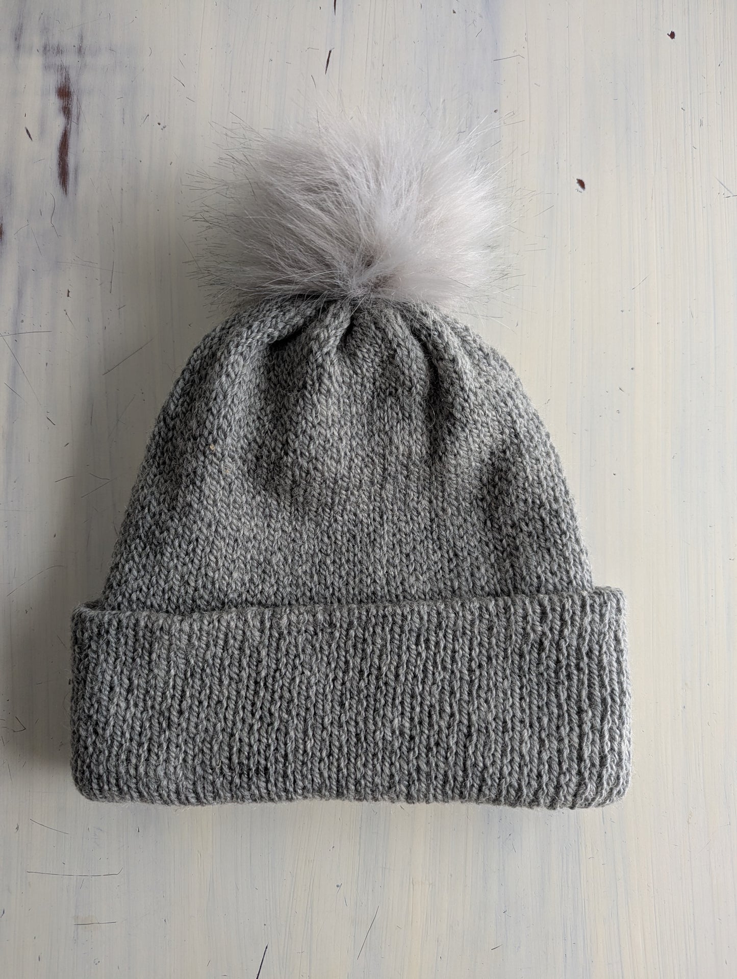 Gray knit beanie with a white pom-pom on a light wooden surface