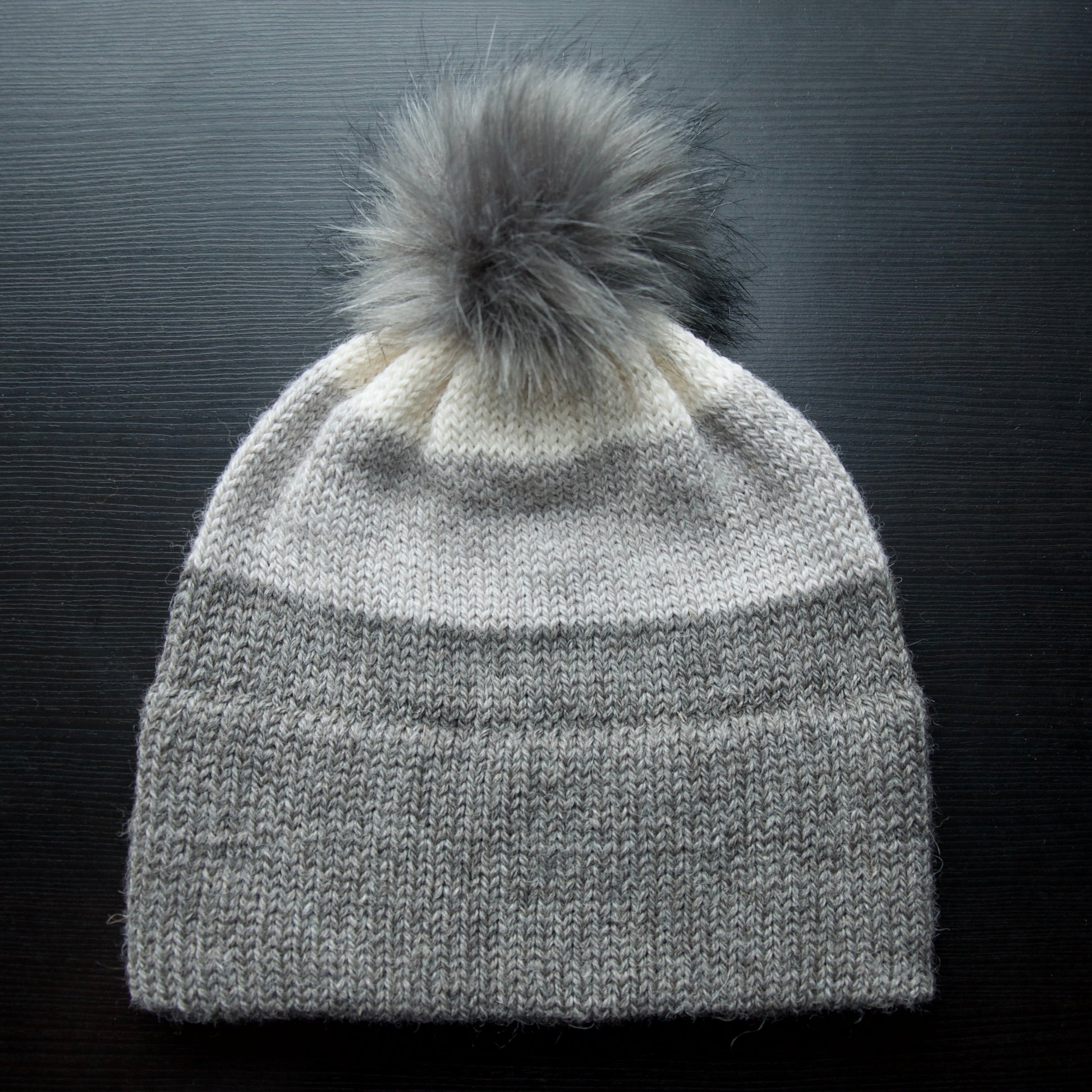 A gray hand stitched hat made with alpaca yarn, featuring a removable pom pom.