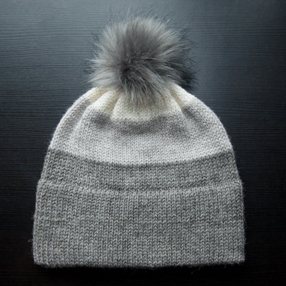 A gray hand stitched hat made with alpaca yarn, featuring a removable pom pom.