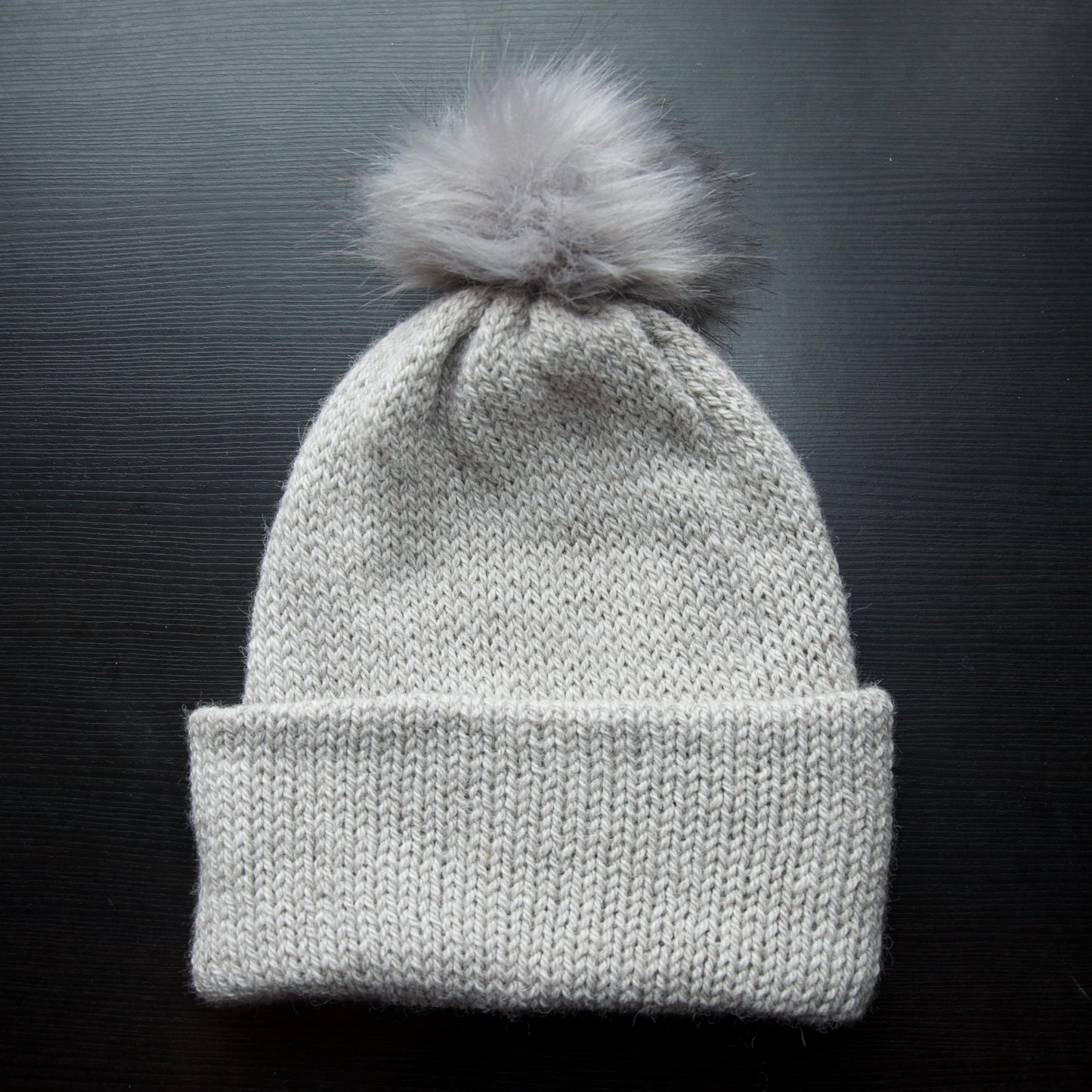 A gray beanie with a removable pom pom on a dark background.