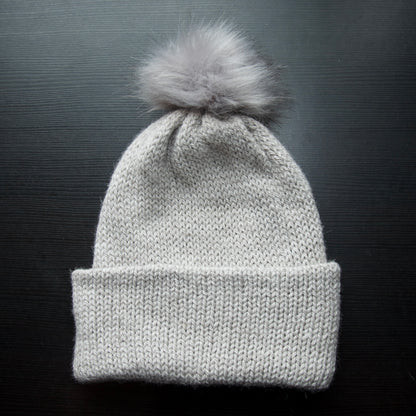 A gray beanie with a removable pom pom on a dark background.