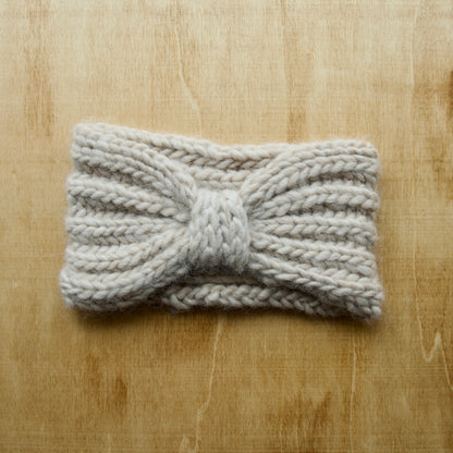 Solid white knit headband with brioche ribbing and a centre piece over a wood background