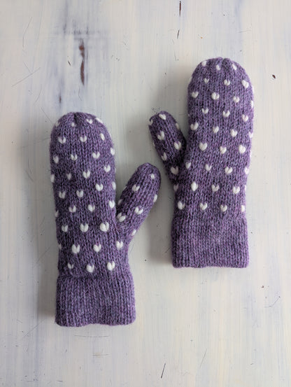 Pair of purple thrun mittens with white hearts on a light wooden surface