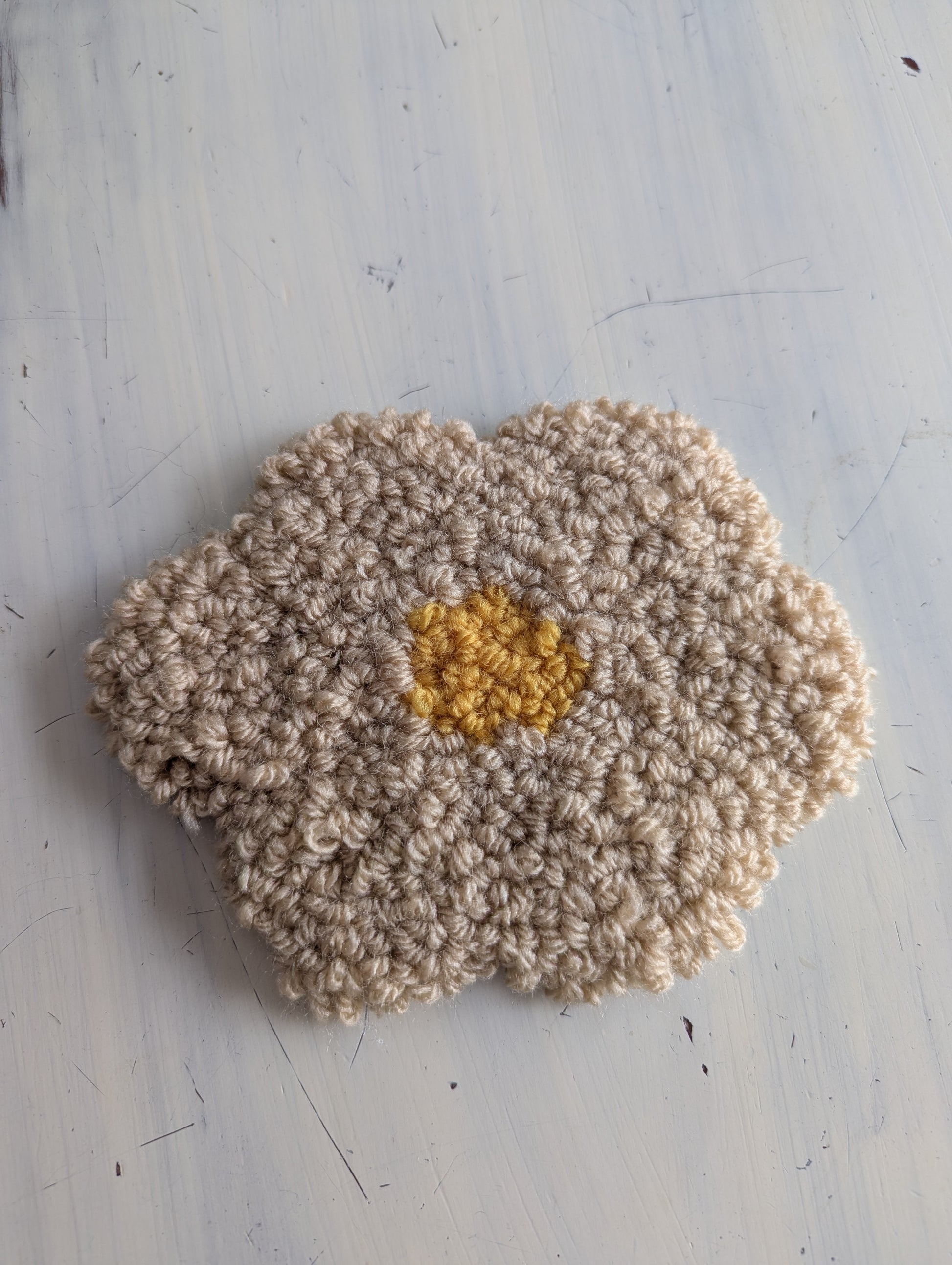 Punch needle flower with beige petals and a yellow center on a light gray background