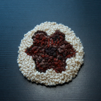 A hand-stitched, circular coaster with a textured red flower in the centre, placed on a dark surface