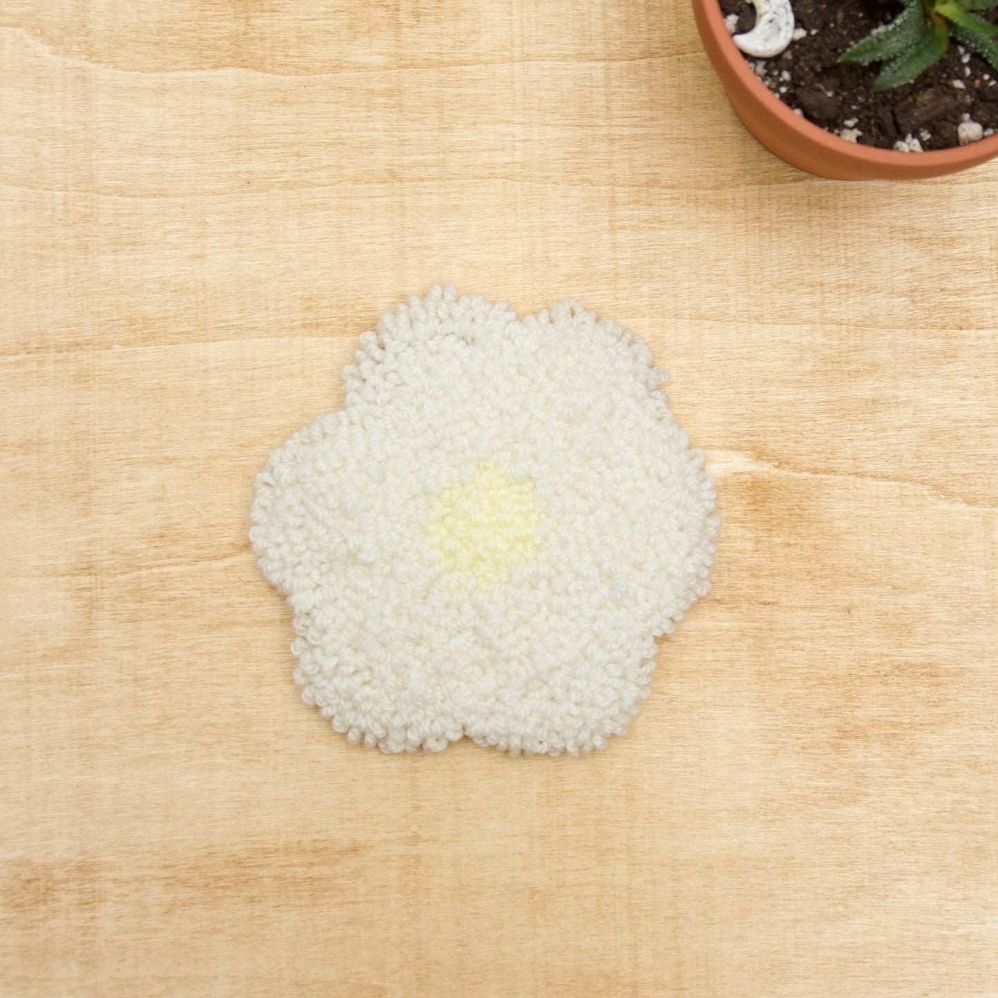 A hand-stitched, punch needle coaster made of various fibers, displayed on a beige background.