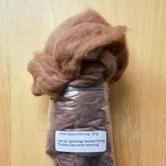 A clear plastic bag filled with brown alpaca roving fiber, with a label indicating it is 30g and used for spinning, needle felting, and weaving.
