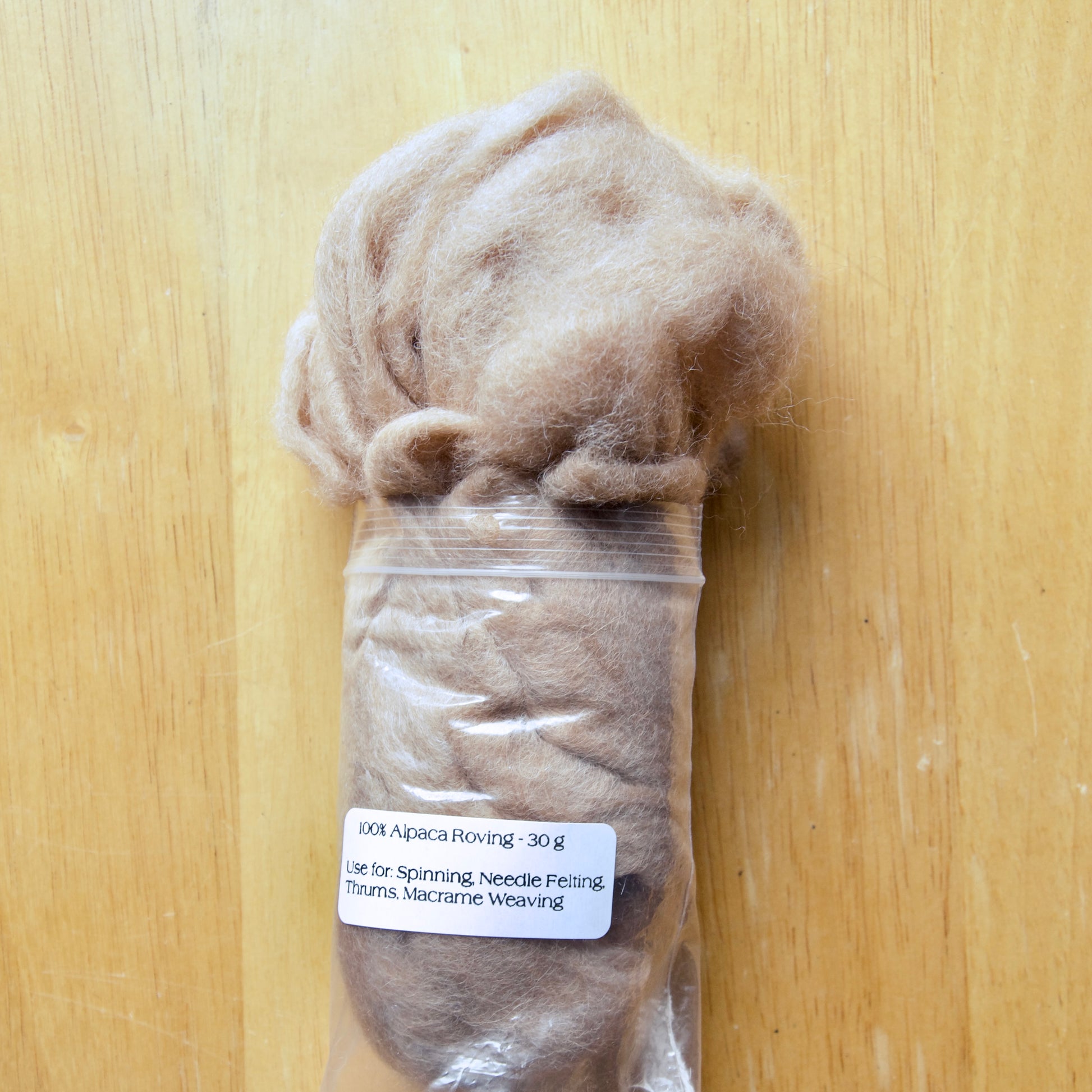 A plastic-wrapped bundle of alpaca roving fiber, 30g weight, displayed on a wooden surface with a label showing the product details.