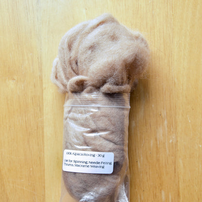 A plastic-wrapped bundle of alpaca roving fiber, 30g weight, displayed on a wooden surface with a label showing the product details.