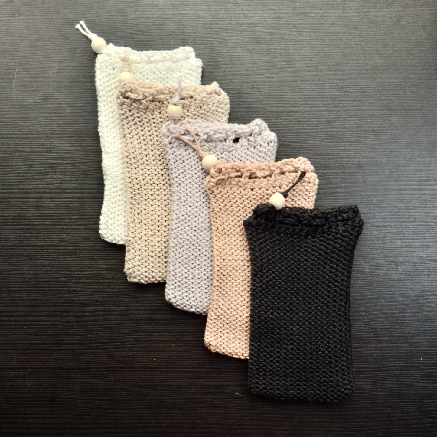 A collection of knit soap saver pouches over a dark surface