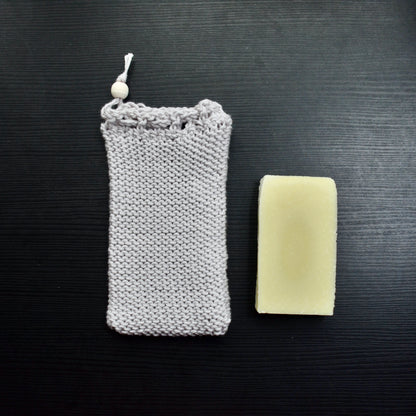 Hand stitched crochet soap saver pouch with a wooden bead, next to a bar of soap.
